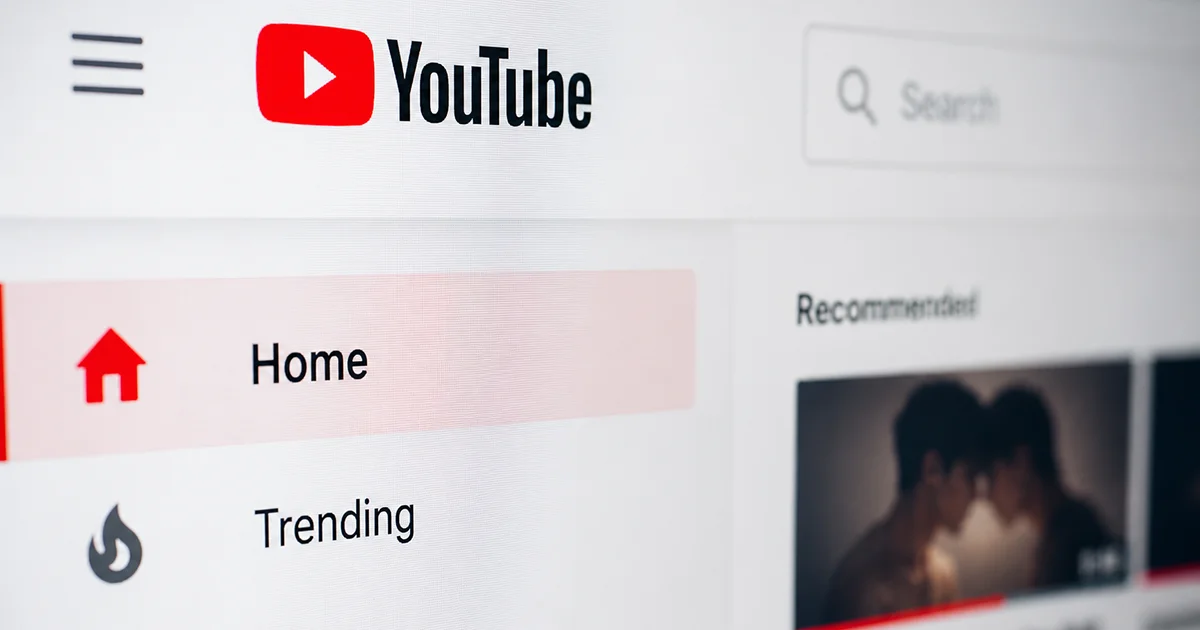 Close-up of the YouTube homepage showing the logo, search bar, navigation menu, and a blurred BL-style video thumbnail.