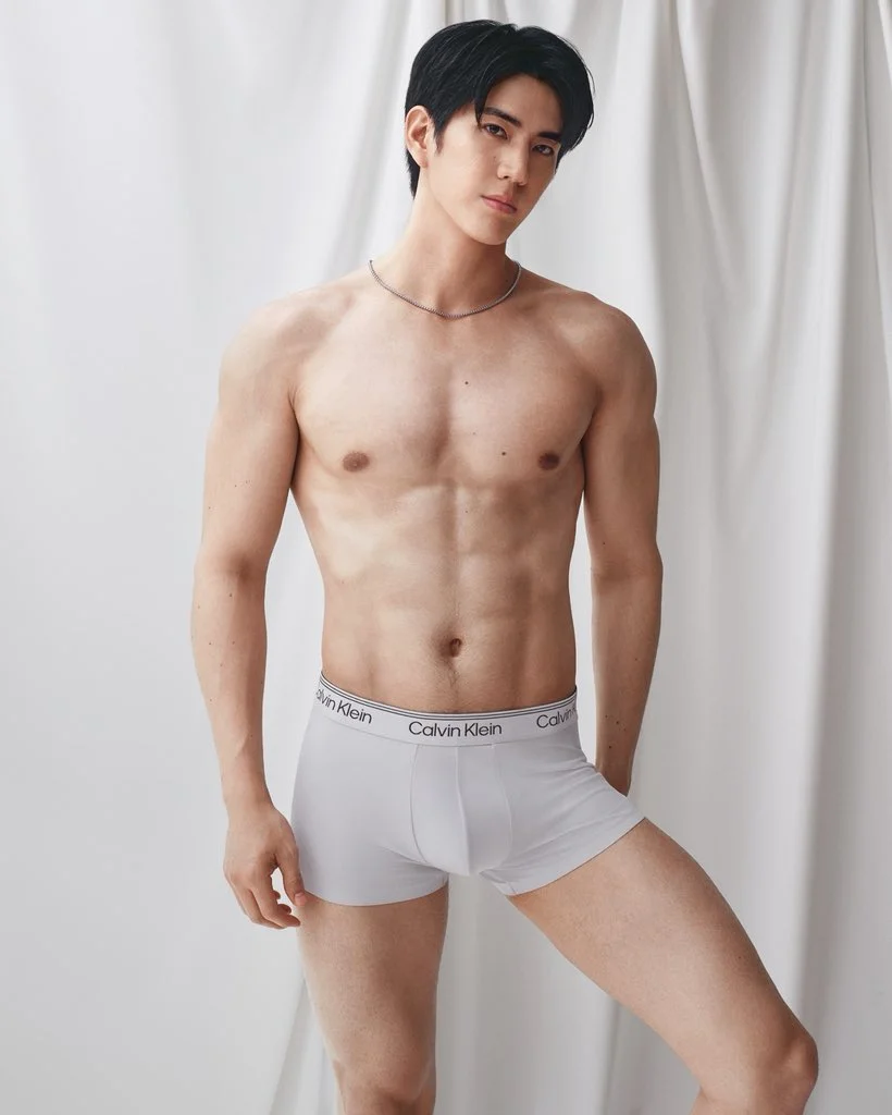 Sea Tawinan poses in white Calvin Klein boxer briefs against softly draped white fabric.