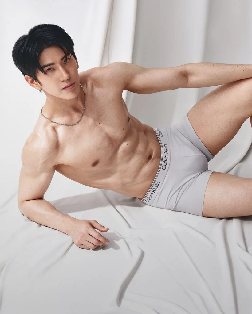 Sea Tawinan reclines on white fabric wearing white Calvin Klein boxer briefs.