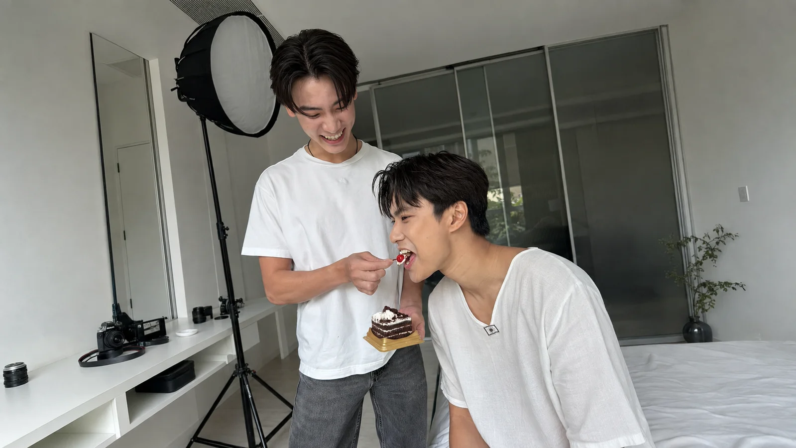 Ing Asavanund smiles as he feeds Ohm Pawat a bite of cake in a photography studio.