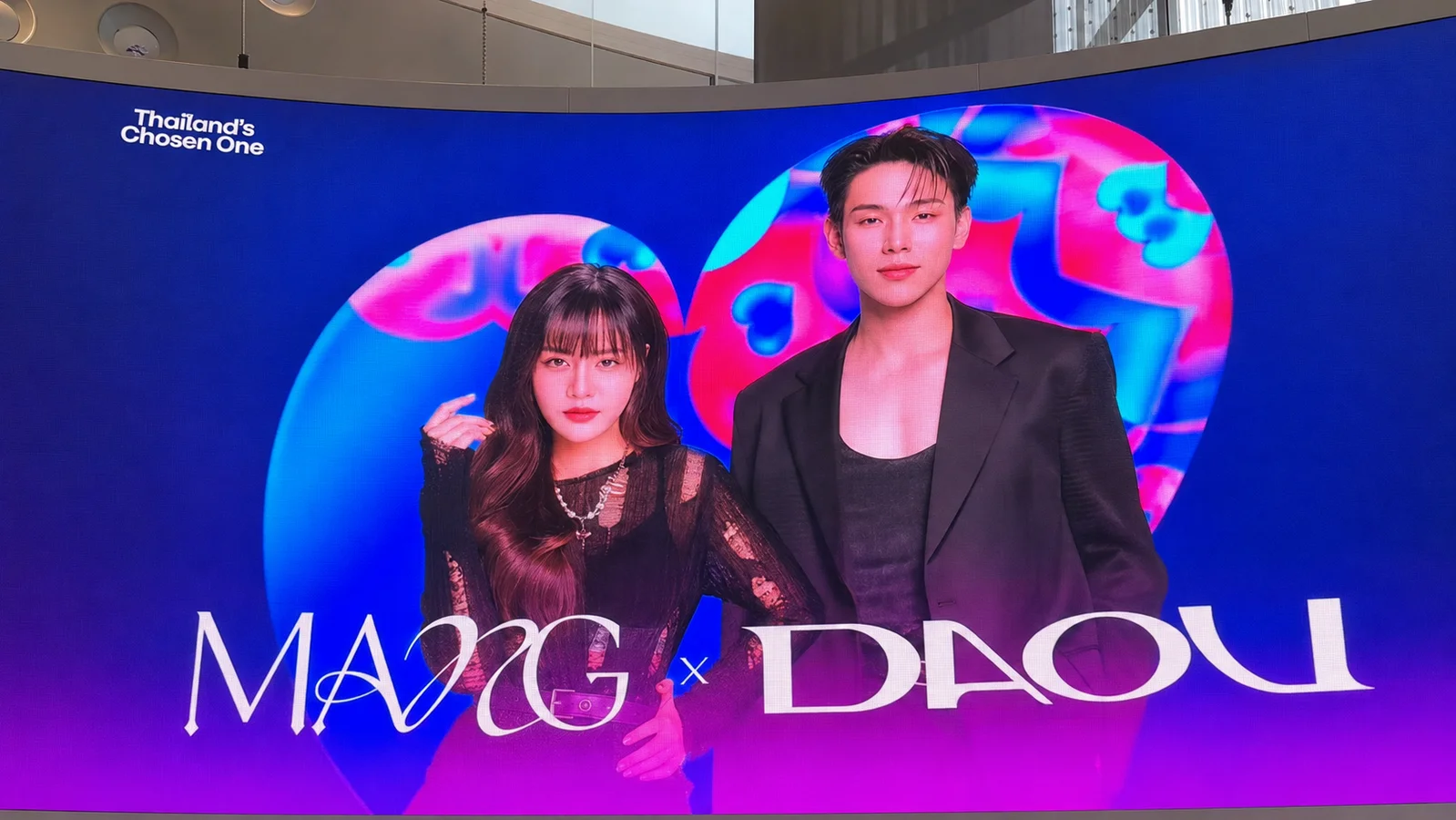MANG and Daou pose in black outfits on a vibrant blue-and-pink promotional screen for Thailand’s Chosen One.