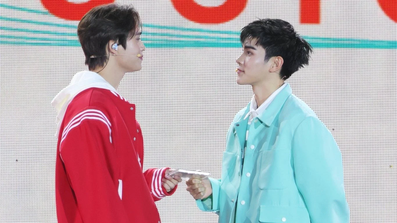 Gemini Norawit and Fourth Nattawat face one another and touch hands while dressed as Tong and Mew during a performance promoting The Love of Siam: The Musical.